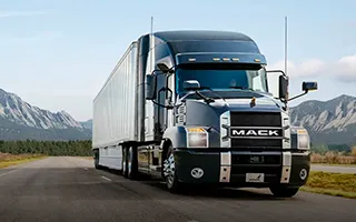 Camion negro Mack circulando en carretera con montañas de fondo